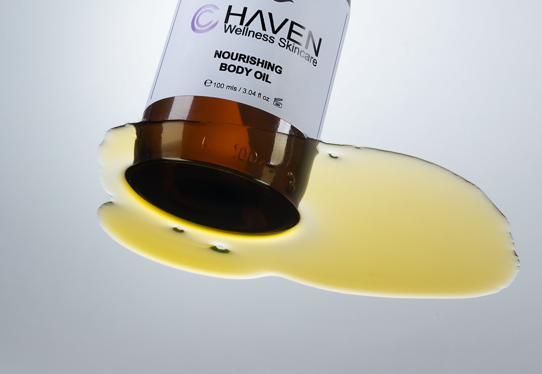 Nourishing body oil pouring from the bottle into a pool on a pale surface